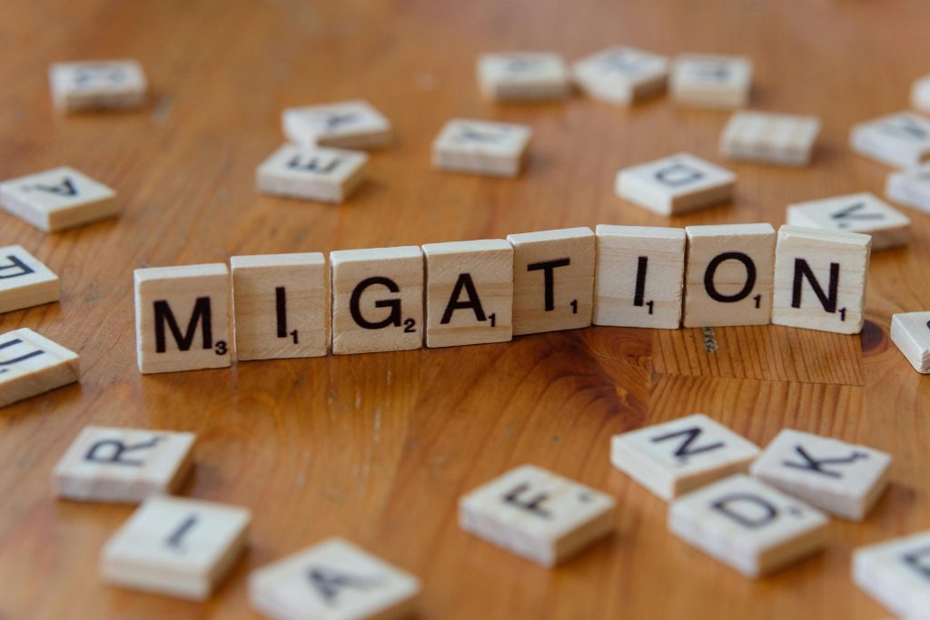 Wooden Scrabble tiles spelling 'Migration' with scattered letters on a wooden table.